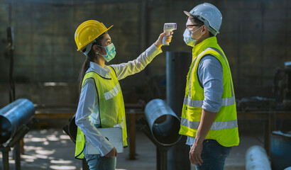 A female engineer is using an infrared thermometer to measure the temperature of workers entering...