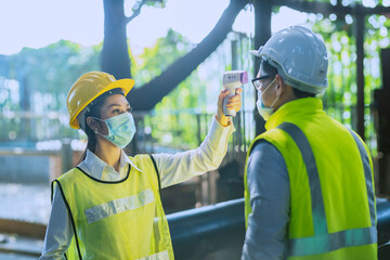 A female engineer is using an infrared thermometer to measure the temperature of workers entering the factory on a daily basis.