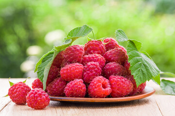 Fresh ripe raspberries in a plate on a wooden table in the garden