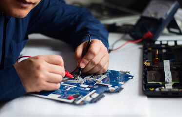 The repairman uses both hands and a meter wire to find the fault on the motherboard on his desk.