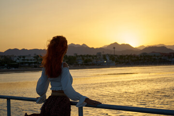 Back view of travel woman with long hair on sea beach at sunset in summer with mountain and Red sea background.eauty woman silhouette at sunset with long healthy wet hair enjoying nature background	