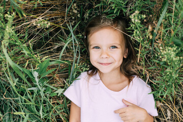 happy little girl in j dress lies in field of wildflowers in summer at sunset. laughs, view from above. lovely cute little girl playing outdoors at sunset, happy childhood