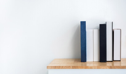 Mockup of white and blue blank book spines on wooden shelf on white background with copy space. Row...