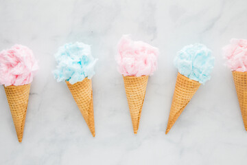 Waffle cones filled with cotton candy all in a row, against a light background.