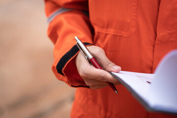 A supervisor in orange coverall is holding luxury ballpoint pen, action to review the paper...