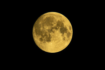 Yellow full moon on dark black sky background, shot from surface of earth with very long telephoto lens. Close-up of moon glowing at clear sky.