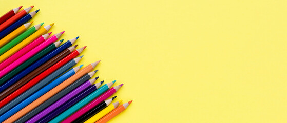 Colored wooden pencils row on yellow background close-up. Set of color pencils with copy space. Banner, top view.
