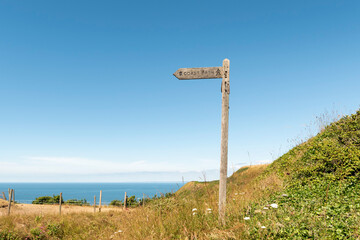 Sign indicating path on hill with sea in the background