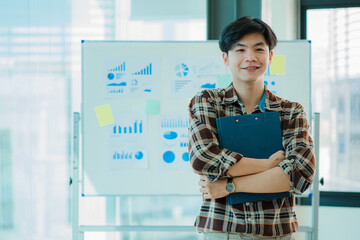 Asian young man Young accountant with file folders standing in office with financial graphs in the...