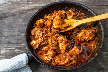 Fried chicken in a frying pan with a wooden spatula on a dark table.