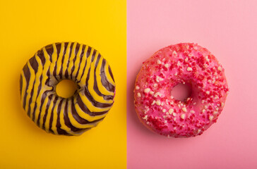 Donuts on a yellow and pink background.Chocolate and strawberry donut with yellow and pink icing on a paper background.Colorful minimalism concept.Junk food.Sweets.Copy space.Flat lay.Place for text.