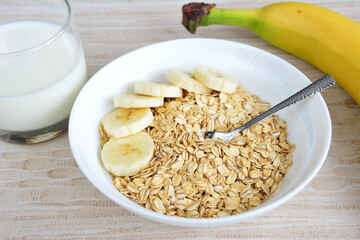 oatmeal with banana slices, teaspoon and glass of milk, close-up