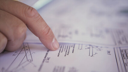 Close up view on engineer hand pointing at technical drawings. Men hands indicating some details in papers, blueprints with building project.