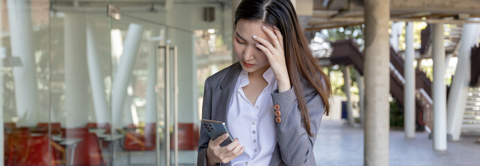 Young woman in a gray suit looks tense over working on a smartphone, Young business woman is stressed by work because the data sent from the smartphone is wrong, Anxious, Sad, Wrong, Depressed.