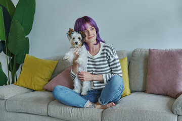 Dreamful teenage girl carrying little dog while relaxing on the couch at home