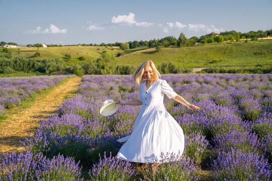 woman model in white dress outfit with hat is standing dancing in lavender field, photo session 
