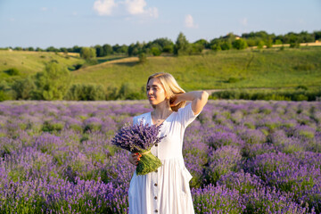 woman model in white dress outfit  is standing in lavender field with bouquet, photo session. Young...
