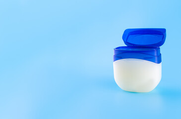 Vaseline or petroleum jelly in a clear jar on blue background with copy space for text. Skin care...