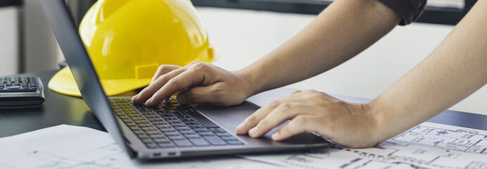 Young man with a laptop plotting a system of building structures in blueprints, Architects or engineers are designing buildings using computers to calculate the physical structure to be correct.