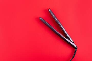 Modern hair iron for straightening on red background, top view with space for text