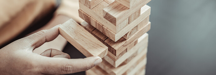 Business growth with wooden blocks concept, Planning to Reduce Investment Risks with Wooden Game Models, hand of a business woman placed a wooden block on a high tower,Management of limited resources. - obrazy, fototapety, plakaty