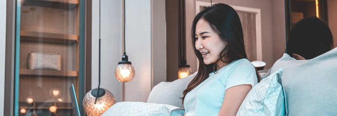 Asian woman uses laptop on bed in modern bedroom at home after she wakes up in the morning,...