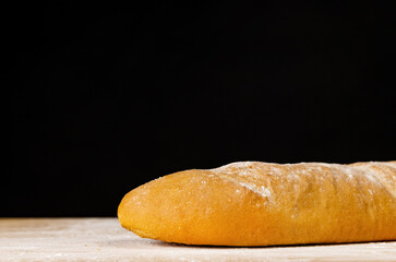 A loaf of bread on a wooden board, dark background. Baguette on wooden board.