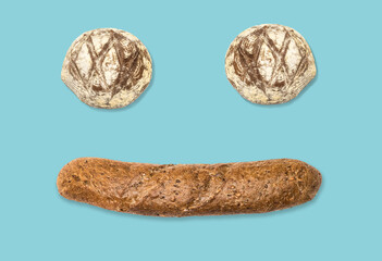 Funny face made of bread buns and dark baguette on blue background. Spun sugar background.