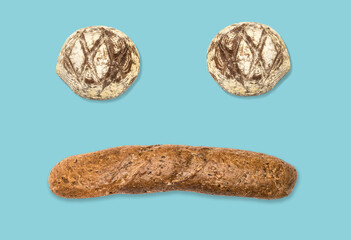 Funny face made of bread buns and dark baguette on blue background. Spun sugar background.