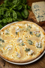 Appetizing baked pizza with white sauce, pear, and gorgonzola cheese on a wooden table. top view