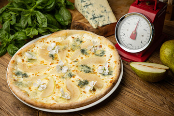 Appetizing baked pizza with white sauce, pear, and gorgonzola cheese on a wooden table. top view