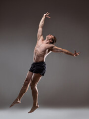 Fototapeta premium Muscular man in an artistic pose, portrait on a gray background. The guy is an athlete in a jump or fall. Expressive pose