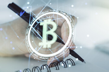 Double exposure of creative Bitcoin symbol with man hand writing in notebook on background. Cryptocurrency concept