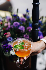 lemon cocktail is held in the hand on the background of flowers