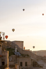 Fototapeta na wymiar Sunrise at Goreme town of Cappadocia, people watching fly of hot air balloons on roofs, fairy chimneys and houses around. Nevsehir, Turkey. 