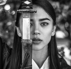 Close-up portrait of an elegant girl lady in form of samurai with steel sword katana female prowess and courage in penetrating look, black and white photo
