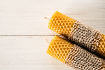 Two handmade honey candles on a white wooden background. Side view, space for text.