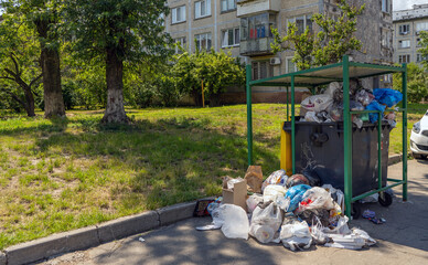 Overflowing garbage can in the city. Huge garbage piles next to the dumpster. Recycling bin...