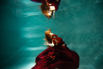 Photo underwater, a young beautiful woman in red with red hair reaches for the surface of the...