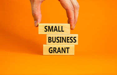 Small business grant symbol. Concept words Small business grant on wooden blocks on a beautiful orange table orange background. Businessman hand. Business, finacial and small business grant concept.
