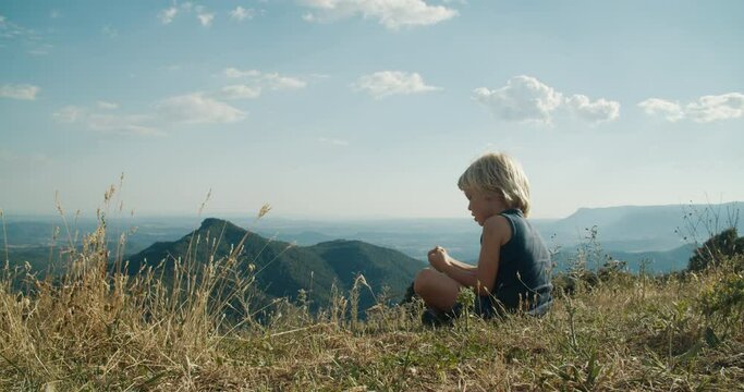 Carefree child sit on top of the mountain enjoy summer vacations on countryside. Children expecting epic landscape on evening during travel. Preschool kid rest on hike journey