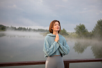 Portrait of young and beautiful woman praying and meditating alone on the sunrise at the coast of...