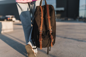 Close-up of tourist women's backpack. Rear view of young woman dressed in denim and with black bag walking down street in city. - 516201999