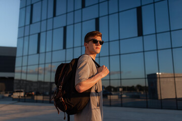 Portrait of handsome tourist hipster man in sunglasses with bag handy, standing guy near the building in downtown. Calm relaxing moment, summer vacation concept - 516202154