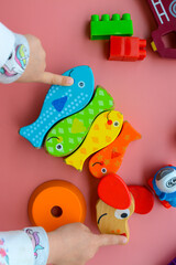 Obraz premium Child is playing with colorful wooden and plastic toys, on pink background