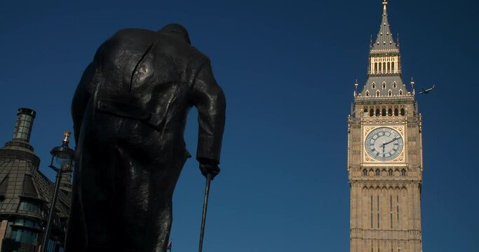 Airplane flying past Big Ben, Houses of Parliament and rear view of the Winston Churchill statue in Parliament Square, Westminster, London, England
