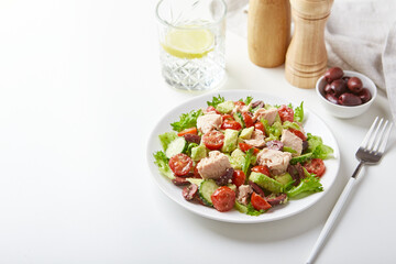 Salad with tuna, lettuce, cucumbers, tomatoes, olives and avocados in white plate on the table