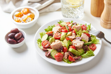 Salad with tuna, lettuce, cucumbers, tomatoes, olives and avocados in white plate on the table