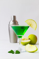 Apple cocktail mixed drink with vodka and apple slice. Apple martini cocktail on the white table. Green Alcoholic drinks in martini glasses with apple slice and shaker. copy space. vertical