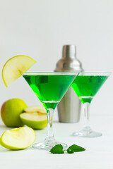 Apple cocktail mixed drink with vodka and apple slice. Apple martini cocktail on the white table. Green Alcoholic drinks in martini glasses with apple slice and shaker. copy space. vertical